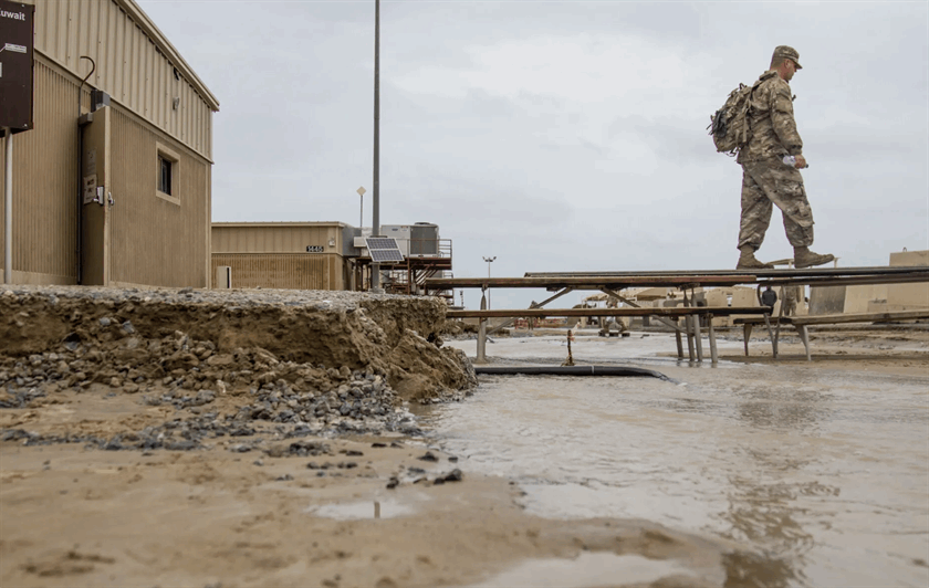 A soldier walks across a makeshift bridge of picnic tables to avoid flood waters at Camp Arifjan, Kuwait, in November 2018.