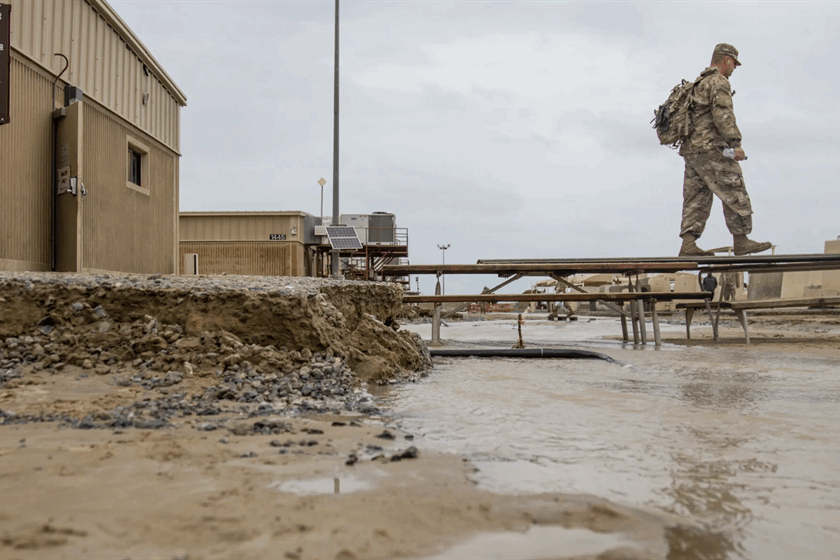 A soldier walks across a makeshift bridge of picnic tables to avoid flood waters at Camp Arifjan, Kuwait, in November 2018.